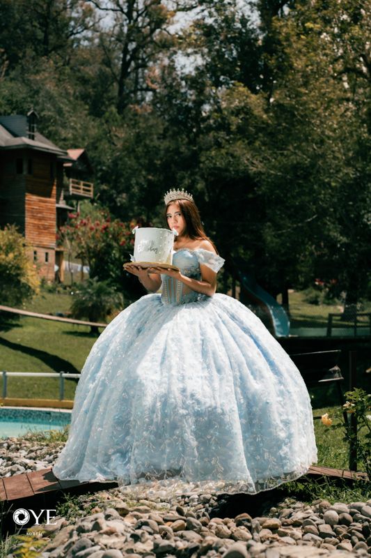 Quinceañera con vestido azul y pastel en el jardín