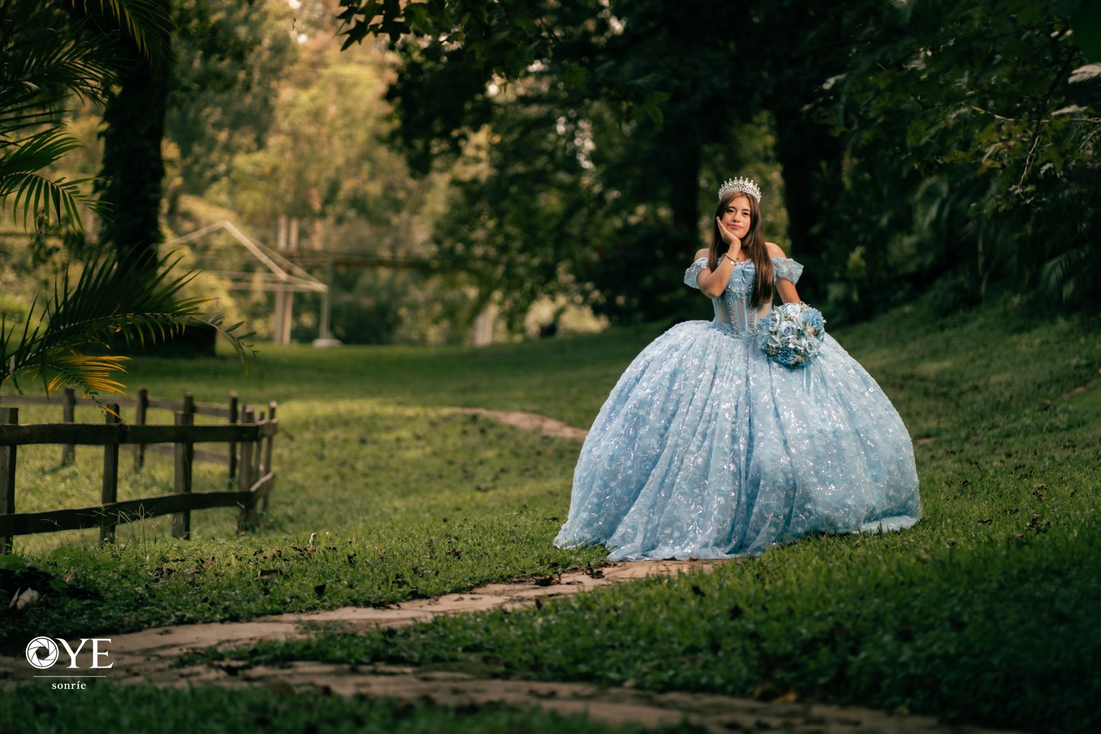 Quinceañera con vestido azul y corona en un jardín